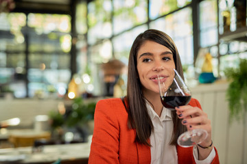 Happy attractive caucasian businesswoman in suit sitting in restaurant for lunch break and drinking red wine.