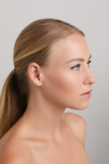 Fototapeta premium Portrait of beautiful young blonde with natural makeup looking aside and posing on white isolated background. Naked female model without accessories in studio. Concept of beauty and tenderness.