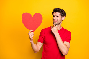 Portrait of doubtful guy celebrate 14-february date get red big paper card heart think disagree...