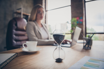 Photo of business woman looking at hourglass counting time till the end of the work day finishing her project in time