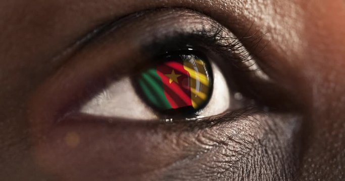 Woman black eye in close up with the flag of Cameroon in iris with wind motion. video concept