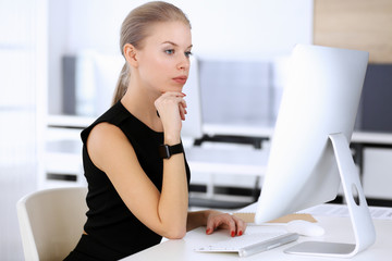 Business woman working with computer while sitting at the desk in modern office. Secretary or female lawyer looks beautiful in black dress. Business people concept