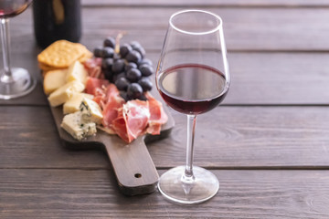 Red wine glass and charcuterie board with different snacks for wine. Different type of cheese, grapes, cured meat and crackers. on wooden table.Wine lover concept