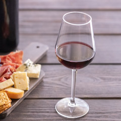 Red wine glass and charcuterie board with different snacks for wine. Different type of cheese, grapes, cured meat and crackers. on wooden table.Wine lover concept