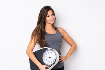 Teenager Brazilian girl holding a scale over isolated white background with arms at hip and holding weighing machine