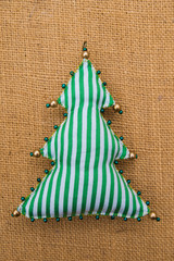 Handmade green striped textile cotton fabric naive retro style Christmas tree ornament decorated with beads on burlap background