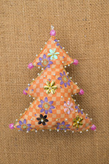 Handmade orange floral  textile cotton fabric naive retro style Christmas tree ornament decorated with beads on burlap background