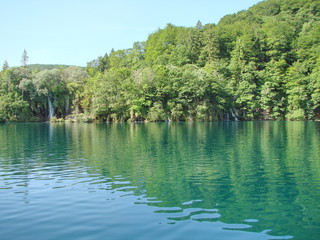 Landscape from the side of the boat to the numerous waterfalls that cover the shores of the forest lake under the rays of the summer noon sun.