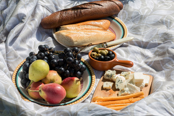 Food for the picnic on light-colored fabric: pears, grapes, olives, bread and some kinds of cheese
