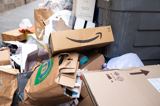 Amazon Prime cardboard box thrown into a pile of trash from a full dumpster.