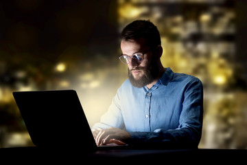 Young handsome businessman working late at night in the office with city lights in the background