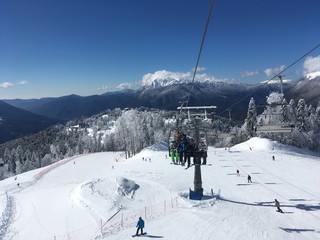 Snowy mountain landscape with trees, bright sun and blue sky with ski run