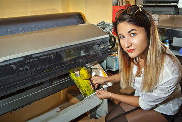 The girl in a white shirt prints a photo. Woman looking through photo with magnifier. The assistant...