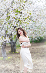 	 A portrait of beautiful young Caucasian woman with curly dark hair in blossoming orchard	