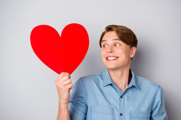 Portrait of cheerful candid guy feel shy cant give big red paper card heart his dream girl girlfriend look wear stylish clothing isolated over grey color background