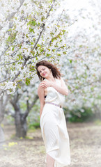 	 A portrait of beautiful young Caucasian woman with curly dark hair in blossoming orchard	
