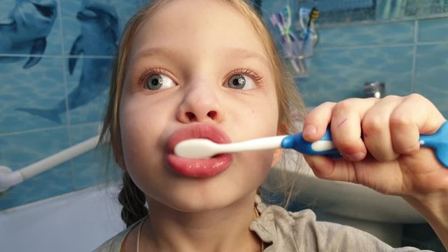 Little girl f brushing her teeth with a toothbrush in bathroom in the morning.