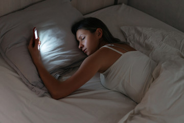 Sleeping woman is holding smartphone in her hand at night. Phone dependence and gadget overuse. Smartphone addiction