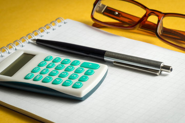 calculator pen Notepad glasses on yellow background