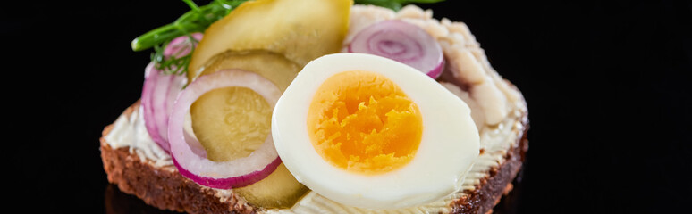panoramic shot of boiled egg on tasty danish smorrebrod sandwich on black