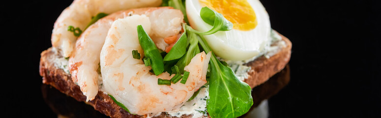 panoramic shot of boiled egg near shrimps on delicious danish smorrebrod sandwich on black