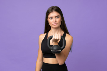Fototapeta premium Young girl woman over isolated background making weightlifting with kettlebell and looking to the front