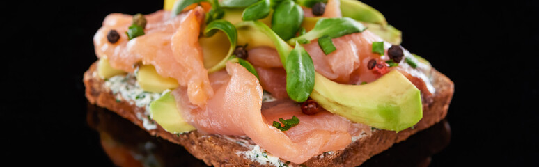 panoramic shot of avocado near salmon on danish smorrebrod sandwich on black