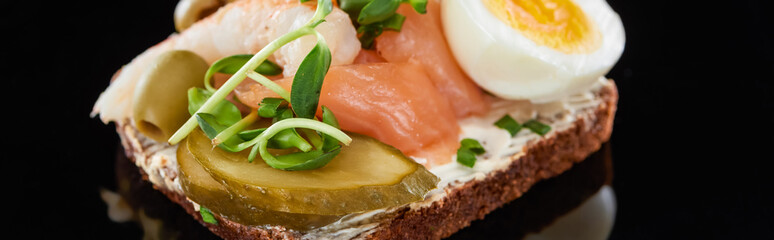 panoramic shot of boiled egg near salmon on danish smorrebrod on black