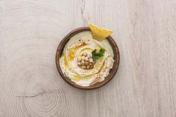 top view of delicious hummus with chickpeas and nacho in bowl on beige wooden table