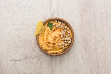 top view of delicious hummus with chickpeas and nacho in bowl on beige wooden table