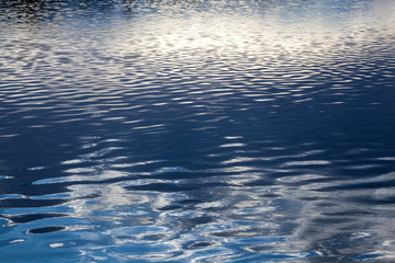 Water surface with sky and sun reflections.