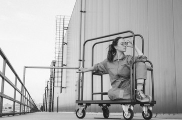 Black and white shot of Young woman in red overalls and red sunglasses having fun on work with shopping cart.
