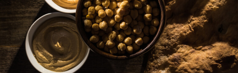 top view of delicious assorted hummus, chickpeas and fresh baked pita on wooden rustic table, panoramic shot