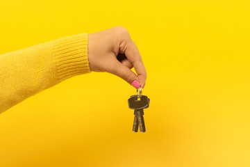 female hand holding house keys, suggesting, over yellow background