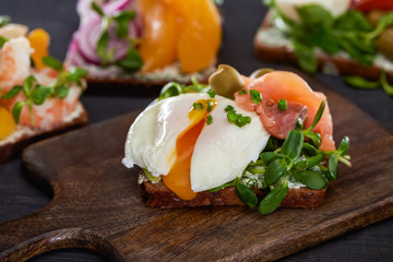 selective focus of danish smorrebrod sandwich with poached egg near salmon on wooden cutting board