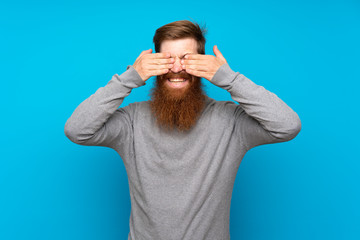 Redhead man with long beard over isolated blue background covering eyes by hands