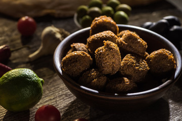 selective focus of delicious falafel balls near lime, black and green olives on wooden rustic table