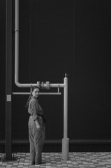 Black and white shot of Young woman in red overalls and red sunglasses posing near gas pipe. Industrial concept