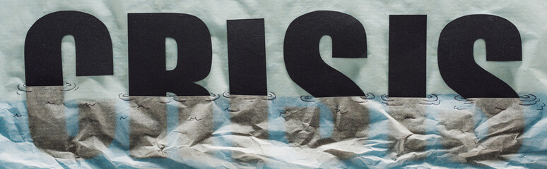 panoramic shot of black word crisis sinking in paper symbolizing water on grey paper background