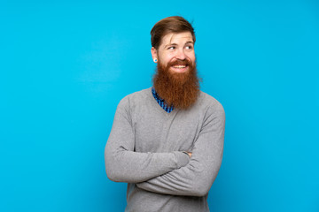 Redhead man with long beard over isolated blue background with arms crossed and happy