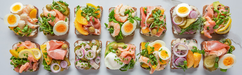panoramic shot of delicious danish smorrebrod sandwiches on white marble surface