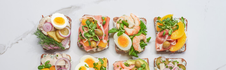 panoramic shot of fresh and tasty smorrebrod sandwiches on white marble surface