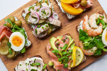 top view of delicious smorrebrod sandwiches on wooden chopping board on white