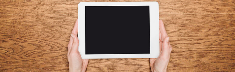 cropped view of woman holding digital tablet with blank screen on wooden desk, panoramic shot