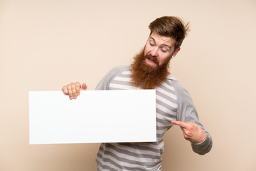 Redhead man with long beard over isolated background holding an empty white placard for insert a concept