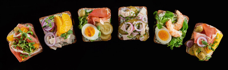 panoramic shot of rye bread with prepared danish smorrebrod sandwiches isolated on black