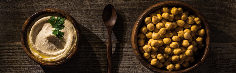 top view of delicious hummus and chickpeas in bowls near spoon on wooden rustic table, panoramic shot