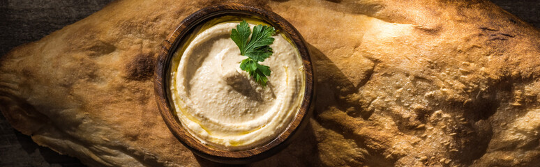 top view of delicious hummus in bowl on fresh baked pita, panoramic shot