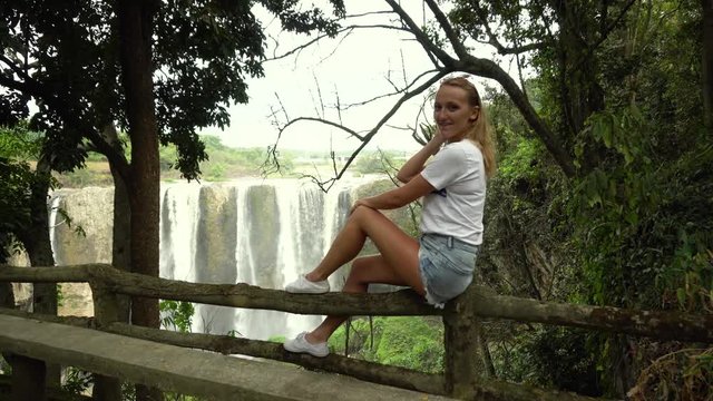 Lovely girl enjoying the view on the waterfall from the bench in the forest.