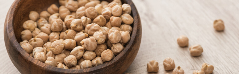 chickpeas scattered from bowl on beige wooden table, panoramic shot